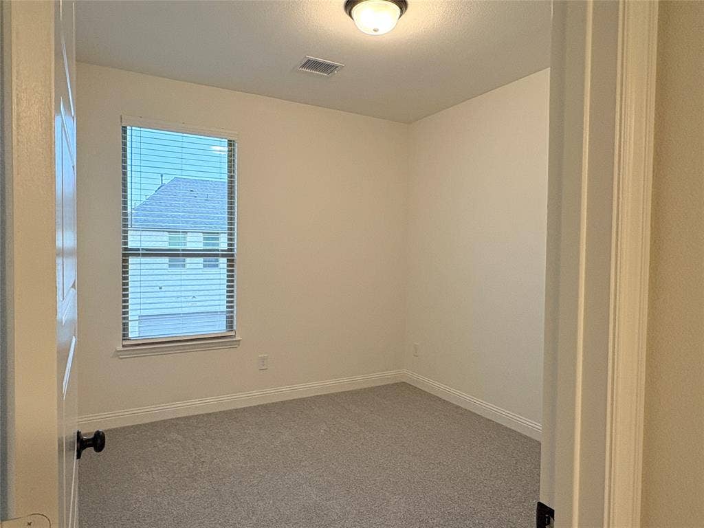 2528 Brunswick Way, Allen, TX 75013 Neutral-toned interior space featuring light-colored wall paint, carpeted flooring, a single window with horizontal blinds, and a central ceiling-mounted light fixture