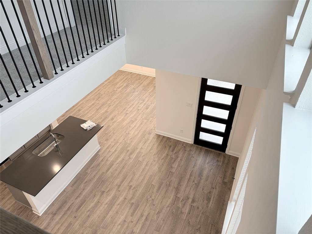 2528 Brunswick Way, Allen, TX 75013 Double-height ceiling with wood-finish flooring, island featuring a built-in sink, and black-framed five-panel entry door with matte black stair balusters