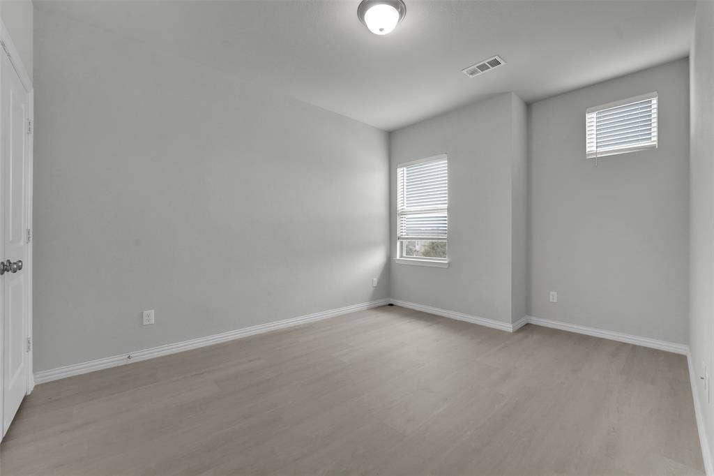 Light wood-finish flooring, two windows with blinds, and white trim