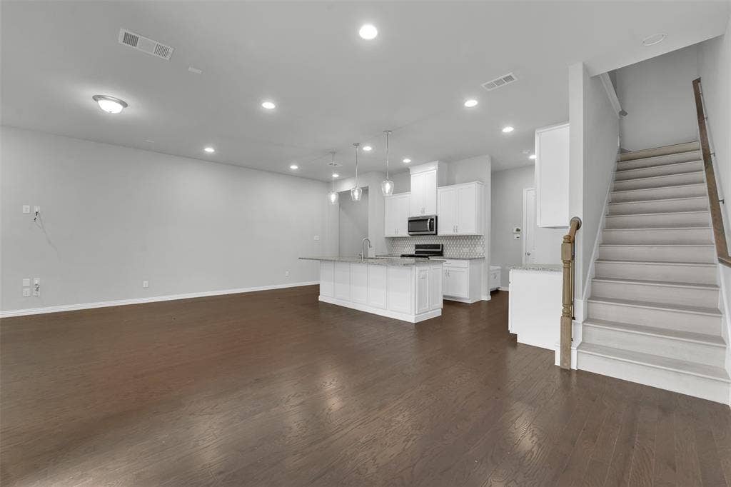Open-concept living area featuring wood-finish flooring, recessed lighting, and a modern kitchen with white cabinetry, stainless steel appliances, and a tiled backsplash