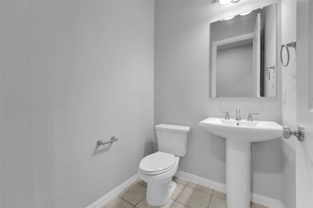 Pedestal sink with chrome faucet, wall-mounted mirror, and tile flooring