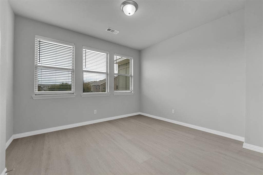 Light gray wood-finish flooring, multiple windows with blinds, and flush-mount ceiling light