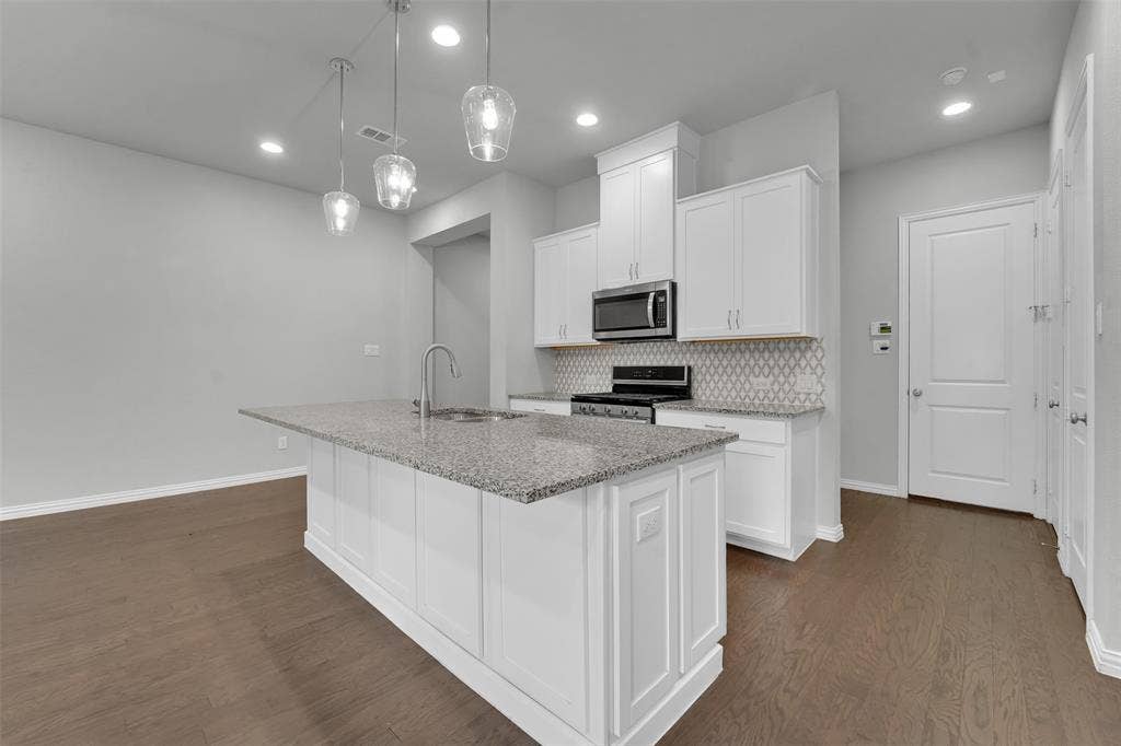 Kitchen featuring wood-finish flooring, a central island with a stone countertop, pendant lighting, white cabinetry, and a patterned tile backsplash