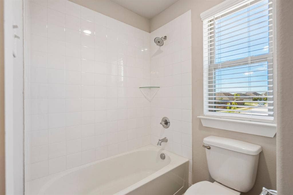 135 Lost Maples Way, Waxahachie, TX 75165 Full bathroom featuring a white tile shower surround, integrated glass corner shelf, chrome fixtures, and a single-hung window with horizontal blinds