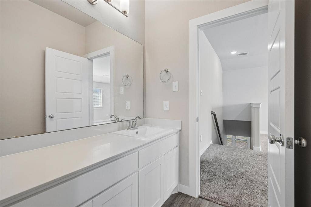 135 Lost Maples Way, Waxahachie, TX 75165 Bathroom featuring a white vanity cabinet, solid-surface countertop with an integrated basin, expansive wall-mounted mirror, polished chrome faucet, and three-bulb vanity lighting fixture