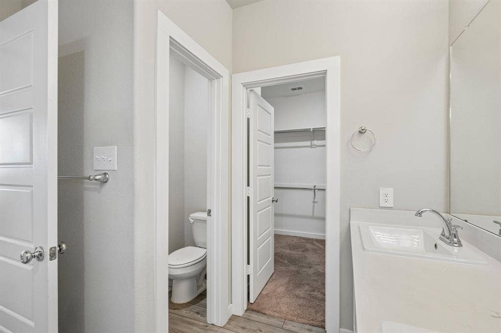 135 Lost Maples Way, Waxahachie, TX 75165 Neutral-toned vanity with an integrated rectangular sink and chrome faucet, large wall-mounted mirror, multiple interior doors with chrome hardware, and dedicated storage area