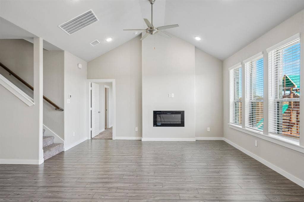 135 Lost Maples Way, Waxahachie, TX 75165 Vaulted ceilings featuring recessed lighting, a modern built-in wall fireplace, wood-finish flooring, and expansive windows with blinds