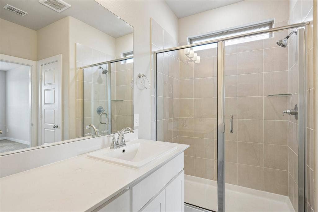 135 Lost Maples Way, Waxahachie, TX 75165 Bathroom featuring a white vanity with a composite countertop, an integrated rectangular sink, a large wall-mounted mirror, and a glass-enclosed shower with tiled walls