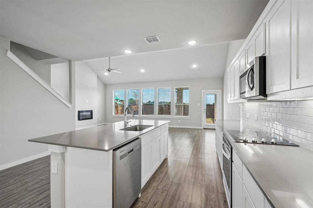 135 Lost Maples Way, Waxahachie, TX 75165 Kitchen featuring white cabinetry, quartz countertops, a subway tile backsplash, stainless steel appliances, and wood-finish flooring under vaulted ceilings