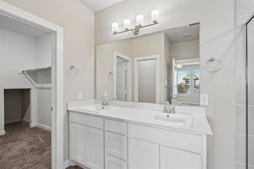 135 Lost Maples Way, Waxahachie, TX 75165 White dual-sink vanity with a solid surface countertop, four-light wall-mounted fixture, and full-width vanity mirror