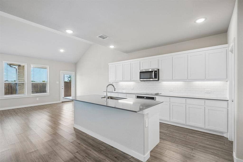 135 Lost Maples Way, Waxahachie, TX 75165 Kitchen featuring white shaker-style cabinetry, quartz countertops, a central island with an integrated sink, subway tile backsplash, and wood-finish flooring