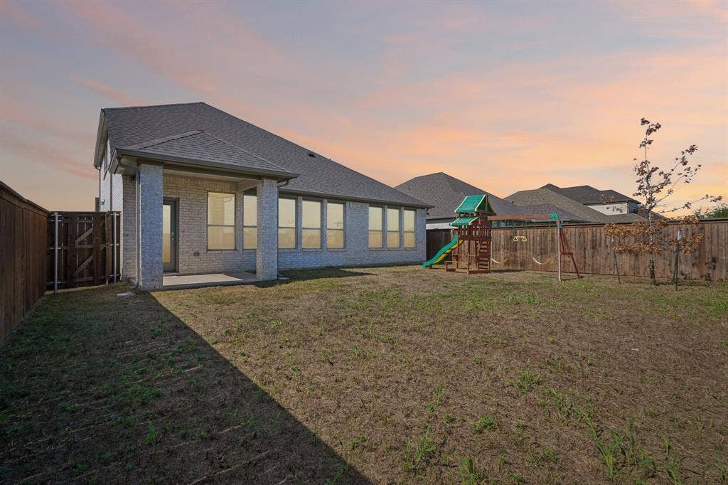 135 Lost Maples Way, Waxahachie, TX 75165 Rear exterior featuring a brick facade, covered patio, large windows, and perimeter wood fencing