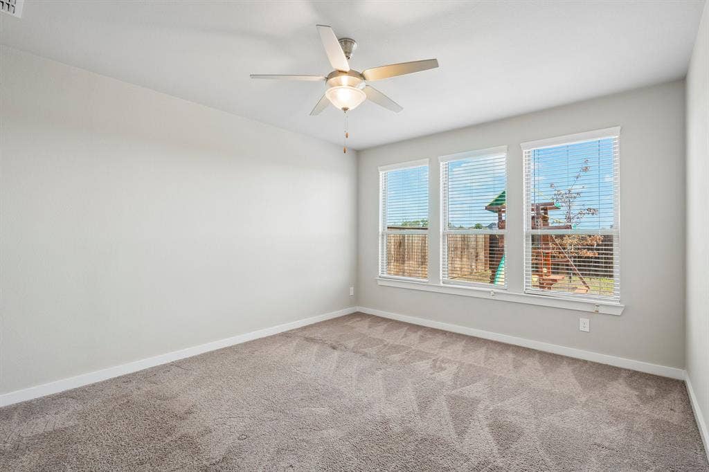 135 Lost Maples Way, Waxahachie, TX 75165 Neutral-toned interior space featuring wall-to-wall carpeting, three windows with horizontal blinds, and a central ceiling fan with an integrated light fixture