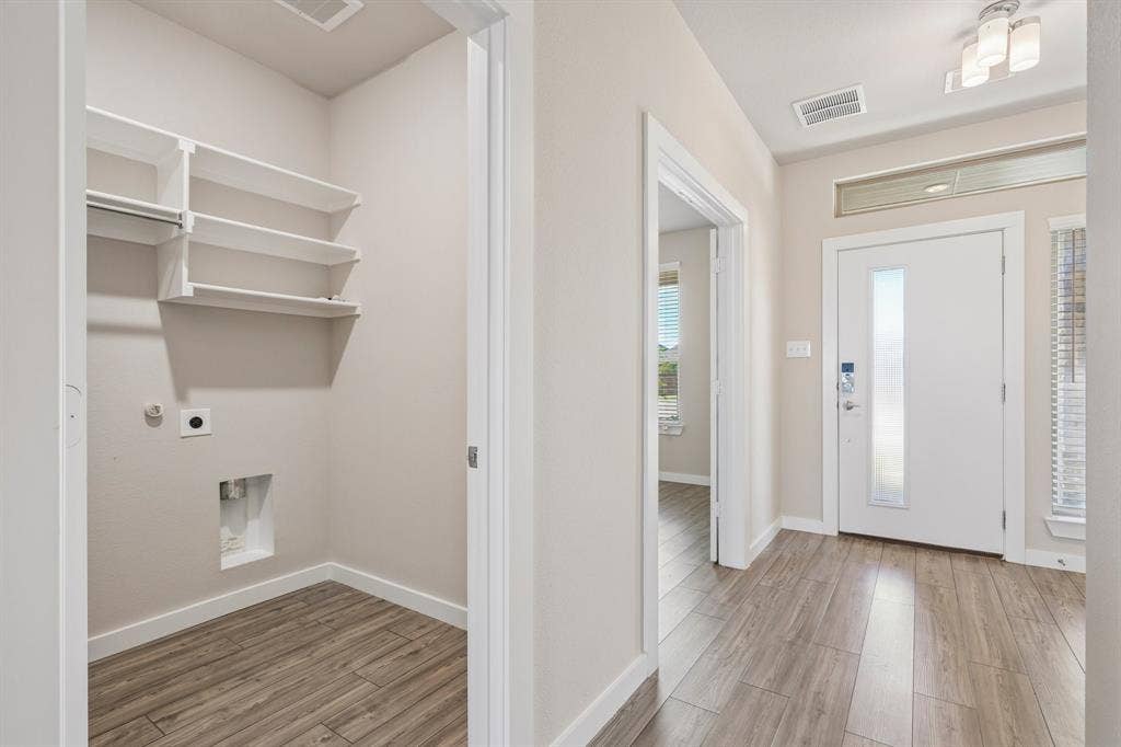 135 Lost Maples Way, Waxahachie, TX 75165 Utility area featuring built-in white shelving, wood-finish flooring, and a white exterior door with a glass insert and transom window