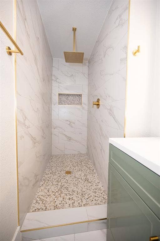 2406 Cliff Teen Court, Dallas, TX 75233 Walk-in shower featuring floor-to-ceiling stone-finish tile, pebble-stone flooring, an integrated tiled niche, a gold-tone rain-style shower head, and gold-tone trim