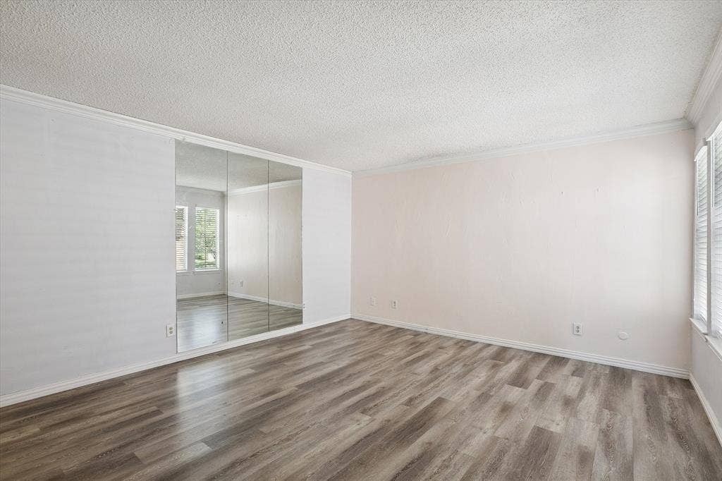 513 Towne House Lane, Richardson, TX 75081 Interior space featuring wood-finish flooring, floor-to-ceiling mirrored wardrobe doors, textured ceilings, and crown molding