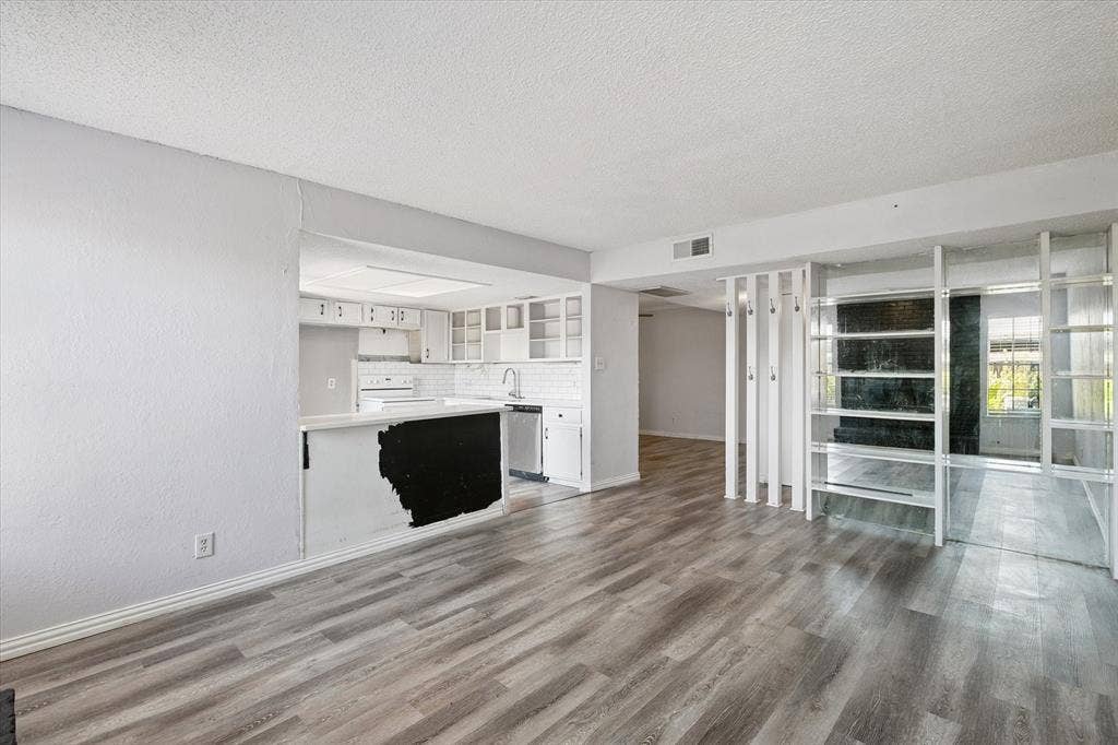 513 Towne House Lane, Richardson, TX 75081 Open-concept interior featuring wood-finish flooring, white cabinetry, a kitchen peninsula, and decorative floor-to-ceiling room partition shelving