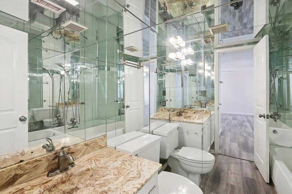 513 Towne House Lane, Richardson, TX 75081 Bathroom featuring floor-to-ceiling mirrored walls, vanity with stone-finish countertop, undermount sink, multi-light fixture, and wood-finish flooring