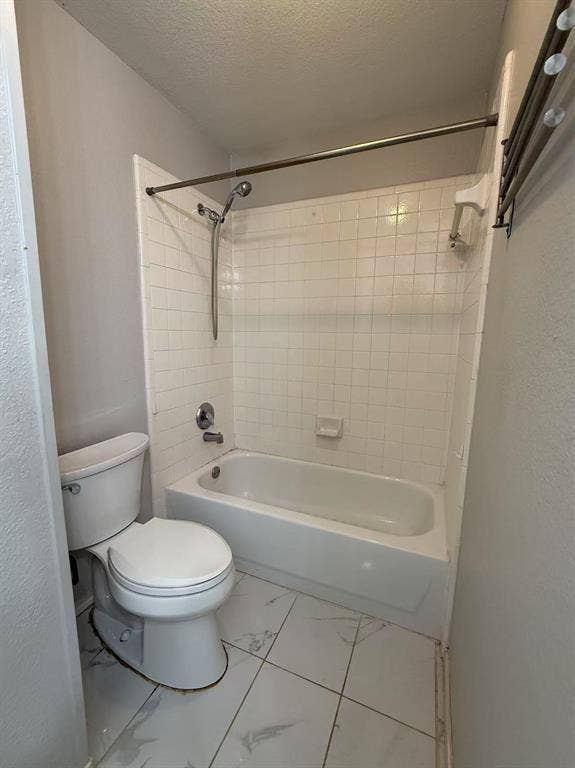 1307 Capstan Drive, Allen, TX 75013 Bathtub and shower combination with white square tile surround, chrome hand-held shower fixture, porcelain toilet, and large-format white tile flooring with grey veining