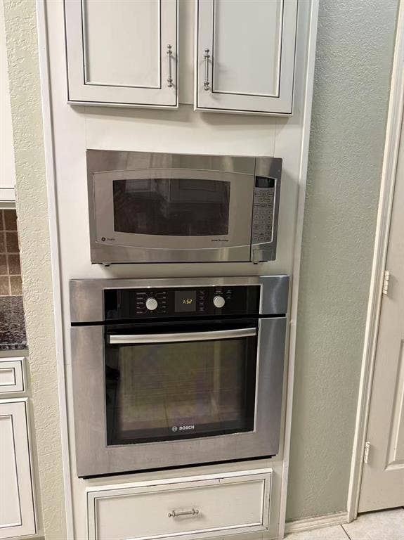 1307 Capstan Drive, Allen, TX 75013 Built-in stainless steel oven and microwave, white shaker-style cabinetry with satin nickel hardware, and lower storage drawer