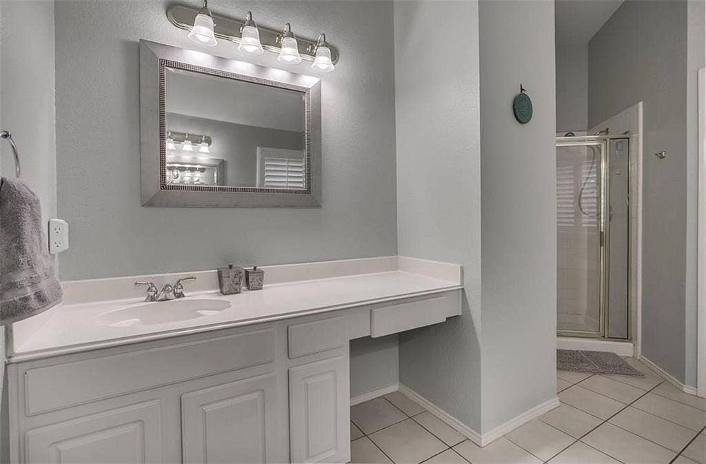 1307 Capstan Drive, Allen, TX 75013 Bathroom featuring a white vanity with an integrated countertop, four-light vanity fixture, framed wall mirror, and a glass-enclosed shower stall with tile flooring
