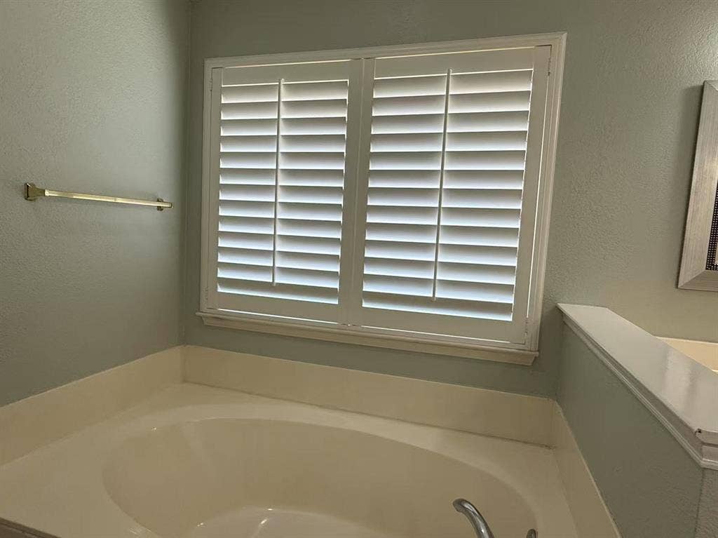 1307 Capstan Drive, Allen, TX 75013 Soaking tub featuring a white surround and polished chrome faucet, paired with white plantation shutters and a wall-mounted metal towel bar