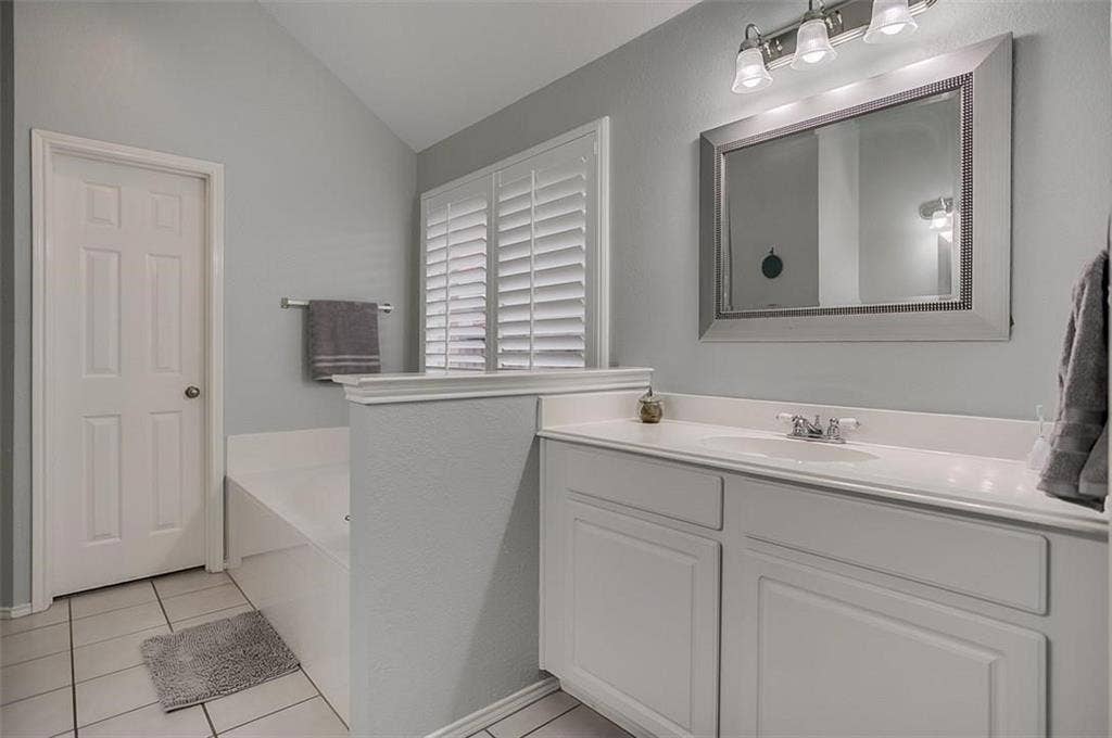 1307 Capstan Drive, Allen, TX 75013 White vanity featuring an integrated sink, vaulted ceiling, white plantation shutters, and a three-light vanity fixture