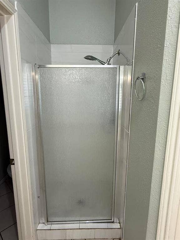 1307 Capstan Drive, Allen, TX 75013 Shower enclosure with a metal-framed glass door, tiled surround, adjustable-height shower head, and wall-mounted towel ring
