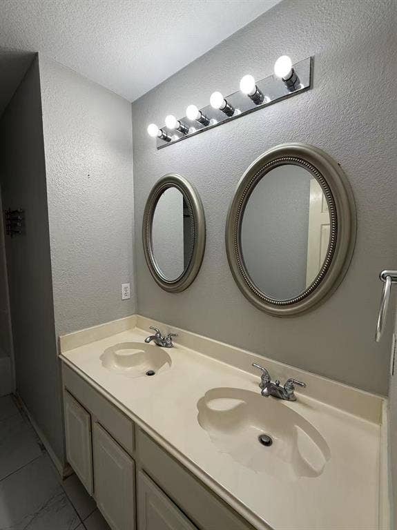 1307 Capstan Drive, Allen, TX 75013 Dual-basin vanity featuring an integrated countertop, two oval wall-mounted mirrors with metallic frames, and a six-bulb vanity light fixture