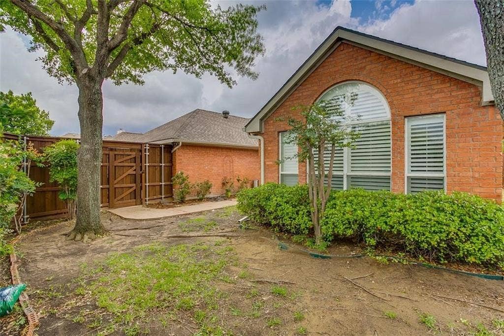 1307 Capstan Drive, Allen, TX 75013 Exterior red brick facade featuring a large arched window with horizontal blinds, a concrete side path, and a wooden privacy fence