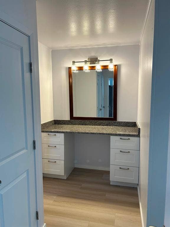 Built-in vanity featuring white cabinetry, stone-finish countertop, wood-finish flooring, a wall-mounted mirror with a dark wood frame, and a four-light fixture