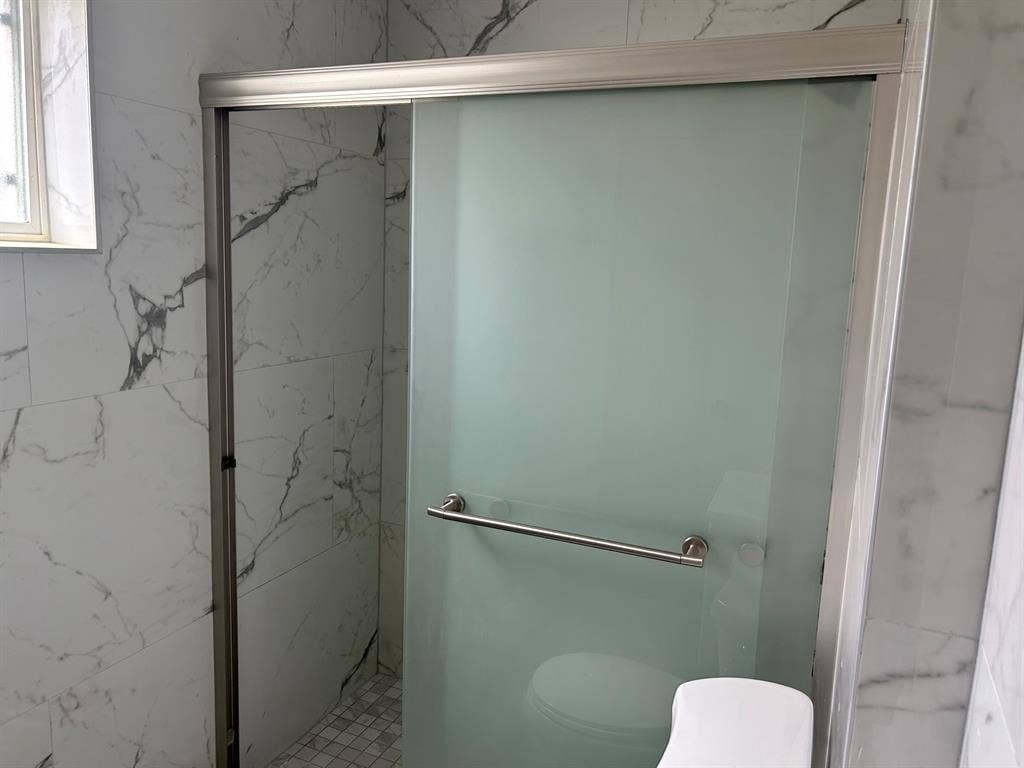 Shower stall featuring large-format wall tile with veining, frosted glass sliding door, brushed metal hardware, and mosaic floor tile