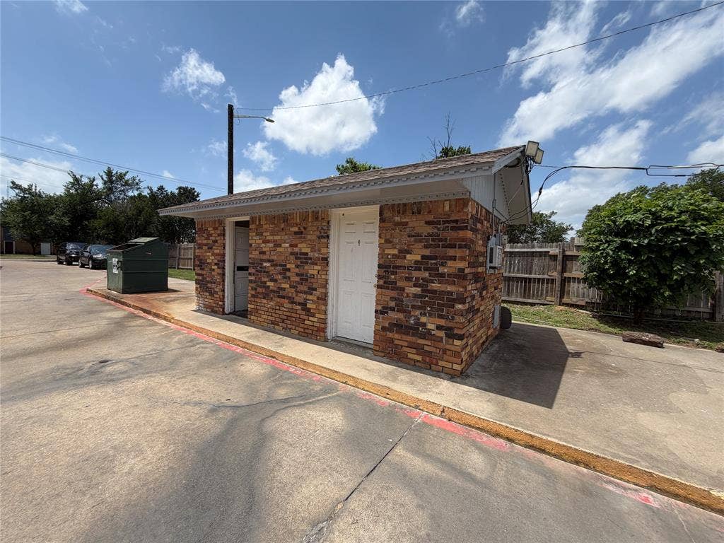 Multi-tone brick exterior featuring a shingle roof, two solid-panel entry doors, and concrete paving