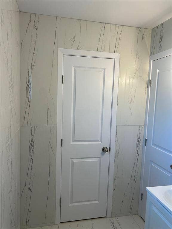 Full-height stone-patterned wall tile, white six-panel interior doors, and matching stone-patterned floor tile