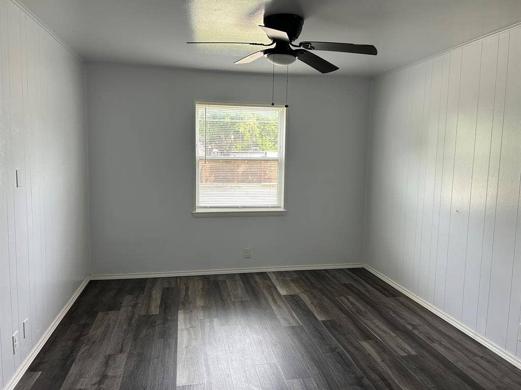 Room featuring wood-finish flooring, vertical paneling, and a ceiling fan with integrated lighting