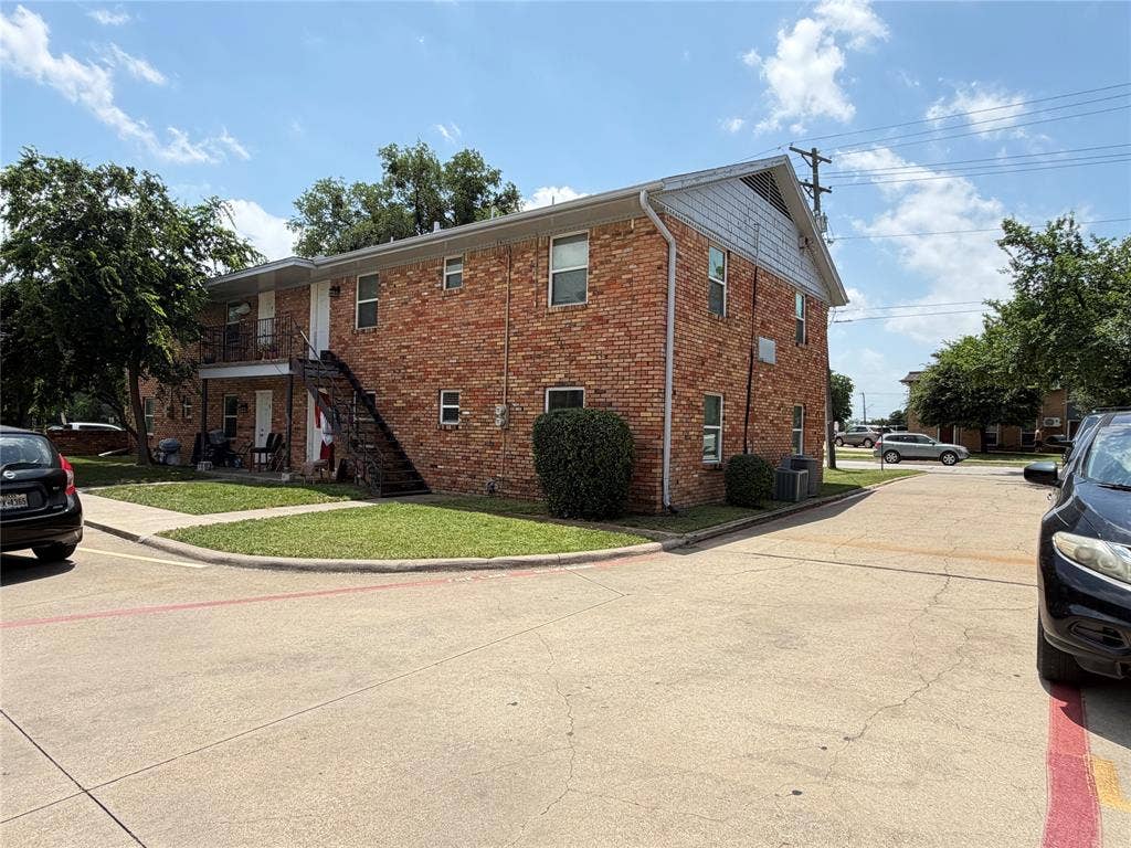 Two-story exterior featuring red brick masonry, siding gable accents, metal staircase, and asphalt parking area