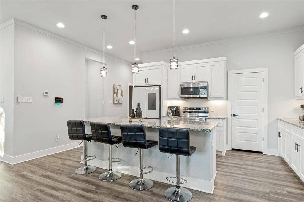 7909 Ivory Lane, Dallas, TX 75216 Kitchen featuring white cabinetry, stone countertops, stainless steel appliances, wood-finish flooring, and three pendant lights suspended over a breakfast bar
