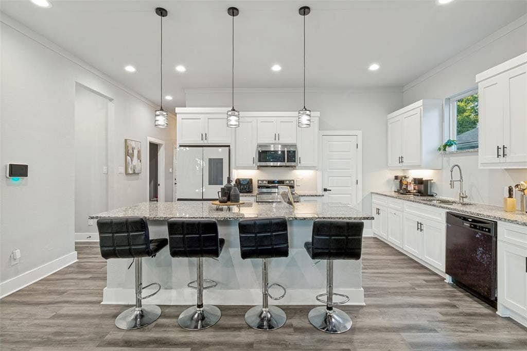 7909 Ivory Lane, Dallas, TX 75216 Kitchen featuring white cabinetry, stone countertops, stainless steel appliances, a center island with bar seating, and wood-finish flooring