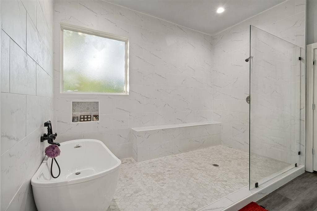 7909 Ivory Lane, Dallas, TX 75216 Freestanding soaking tub with a wall-mounted faucet, walk-in shower featuring a built-in bench, glass enclosure, and floor-to-ceiling stone-patterned wall tile