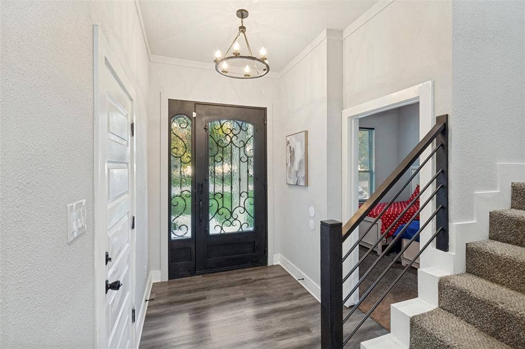 7909 Ivory Lane, Dallas, TX 75216 Entryway featuring a dark-finish iron-accented front door, wood-finish flooring, a tiered metal chandelier, and a staircase with a horizontal rail system