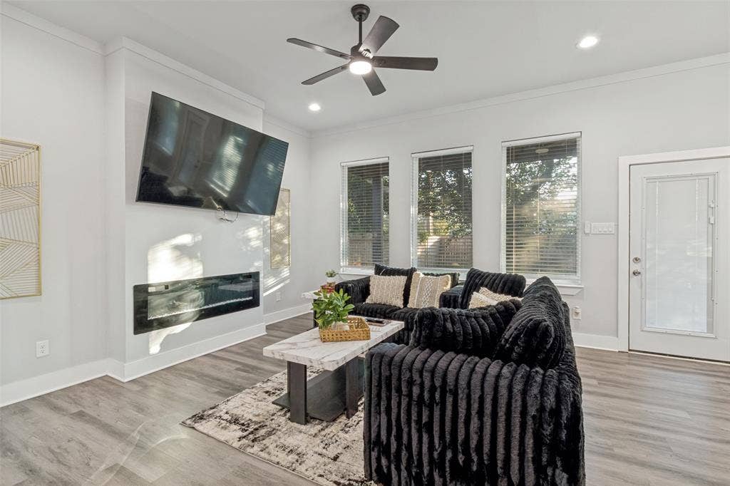 7909 Ivory Lane, Dallas, TX 75216 Living area featuring wood-finish flooring, a contemporary recessed linear fireplace, three windows with blinds, a modern ceiling fan, and a glass-paneled exterior door