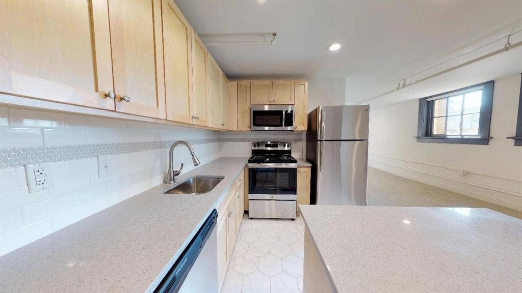 Kitchen featuring light brown cabinets, tasteful backsplash, light stone countertops, appliances with stainless steel finishes, and sink
