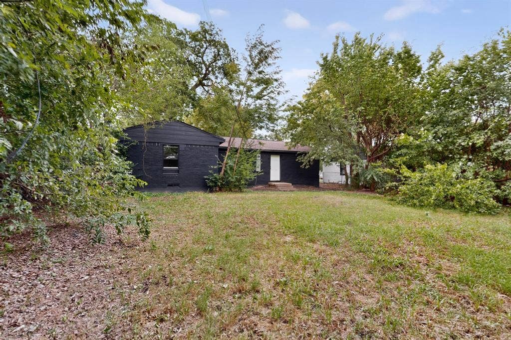 1831 Highland Street, Mesquite, TX 75149 Exterior featuring a dark-painted brick facade, gabled roofline, and expansive grounds with mature trees