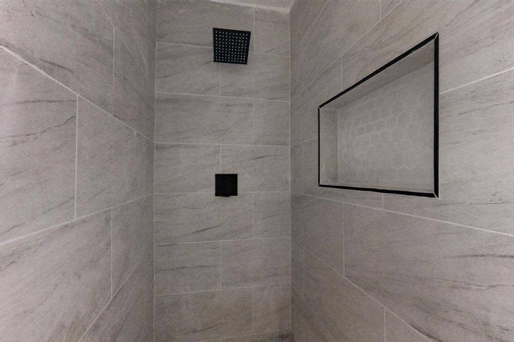 1831 Highland Street, Mesquite, TX 75149 Walk-in shower featuring large-format light grey stone-patterned tile, matte black rain-style shower head, matte black single-handle mixing valve, and a recessed wall niche with a contrasting border