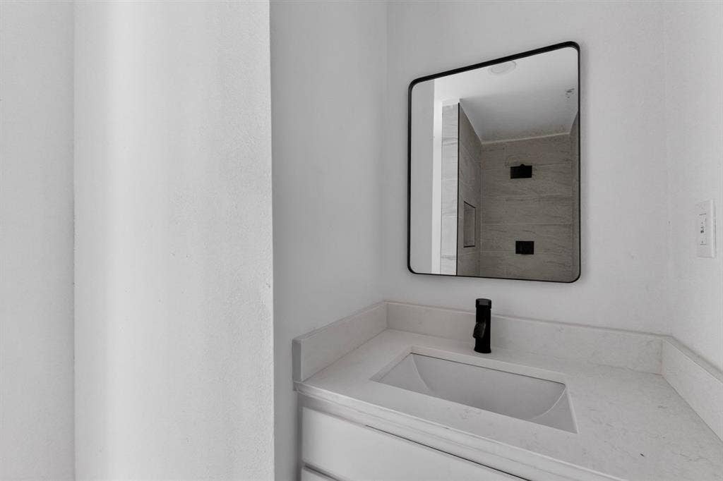 1831 Highland Street, Mesquite, TX 75149 Vanity featuring a solid-surface countertop with an integrated rectangular sink and matte black faucet, paired with a square-cornered mirror in a black frame