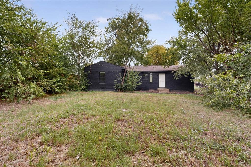 1831 Highland Street, Mesquite, TX 75149 Exterior featuring a black brick facade, gable roofline, and mature trees situated on a grass-covered lot