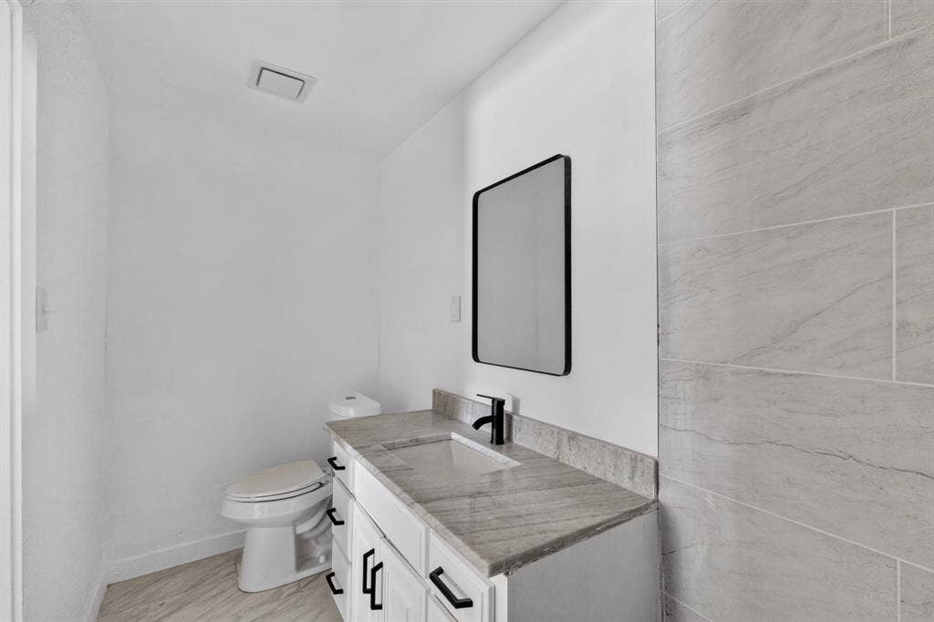1831 Highland Street, Mesquite, TX 75149 Bathroom featuring white cabinetry, stone-finish countertop, rectangular under-mount sink, matte black hardware, and large-format wall tile