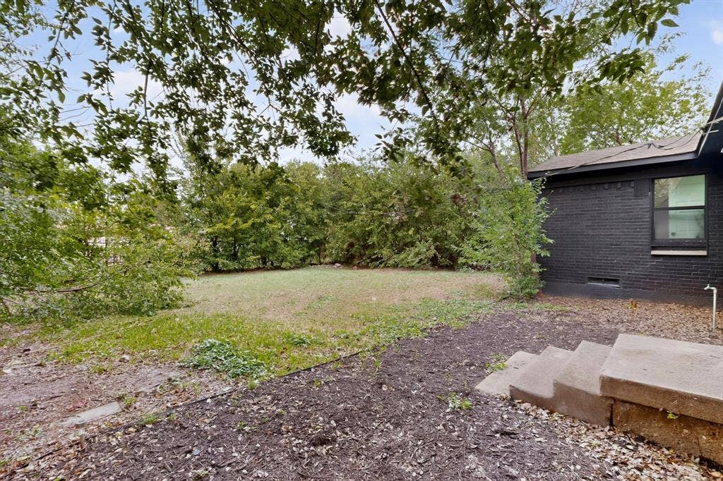 1831 Highland Street, Mesquite, TX 75149 Backyard featuring a grass lawn, mature trees, concrete steps, and a dark-toned brick exterior