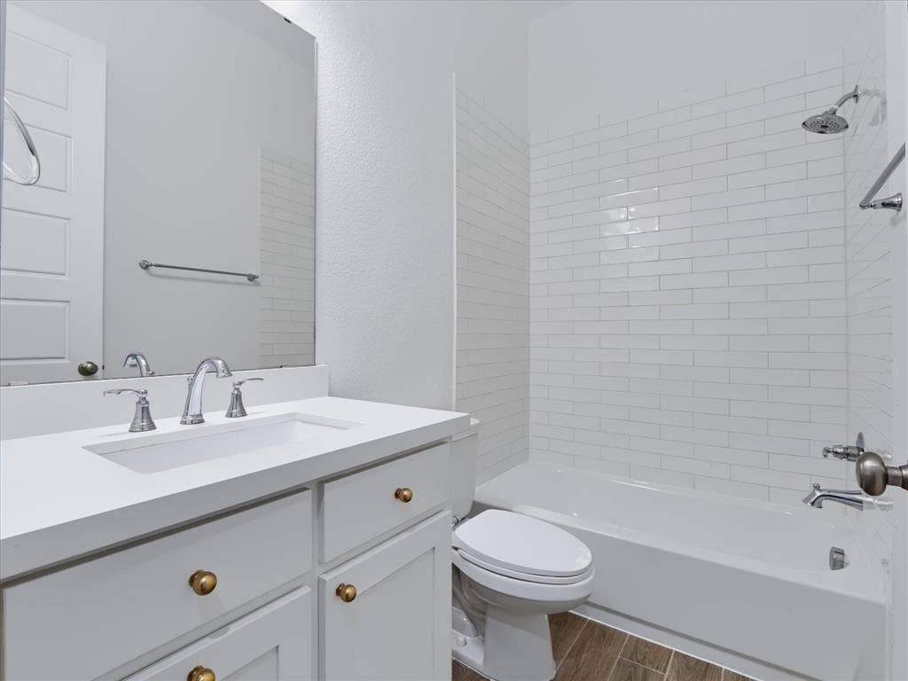 1103 Sandgate Drive, Forney, TX 75126 Bathroom featuring a white vanity with a composite countertop, undermount sink, brass hardware, subway tile tub surround, and wood-finish flooring