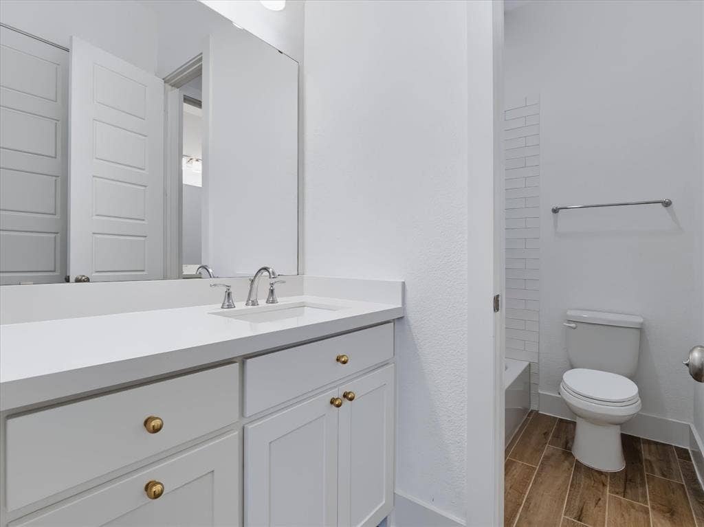 1103 Sandgate Drive, Forney, TX 75126 White vanity cabinet with brass-tone hardware, white countertop with integrated sink, polished chrome faucet, wood-finish flooring, and white subway tile wall accents